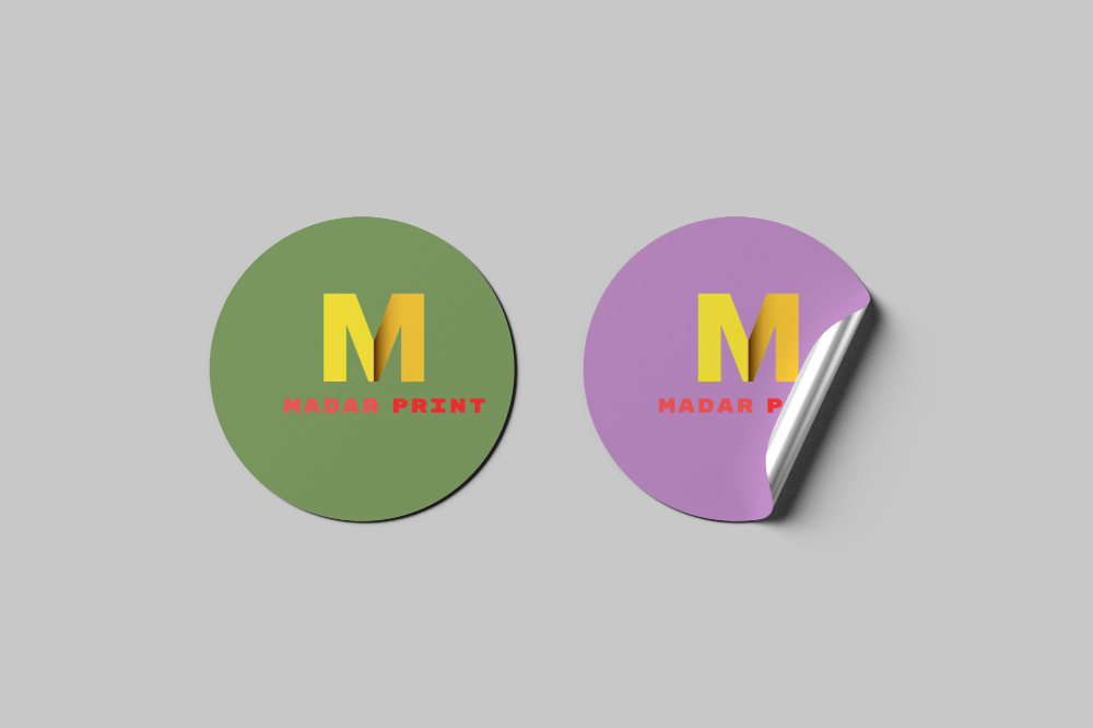 Set of two round stickers: green and purple with bold 'M' and 'Madar Print' logo.